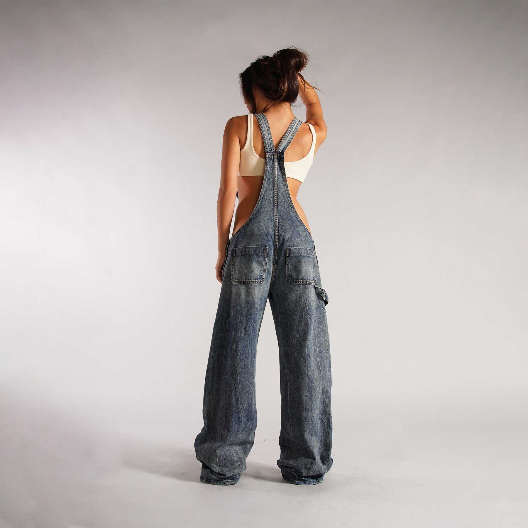 Back view of a woman wearing wide leg zipper denim overalls with pockets and high waist design